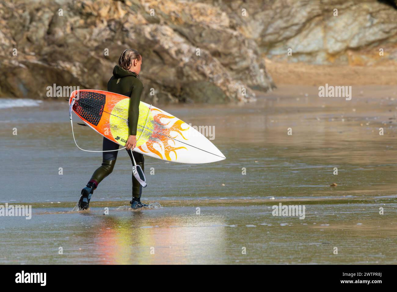 Ein junger Surfer mit seinem Surfbrett nach einer Surfsession in Fistral in Newquay in Cornwall, Großbritannien. Stockfoto