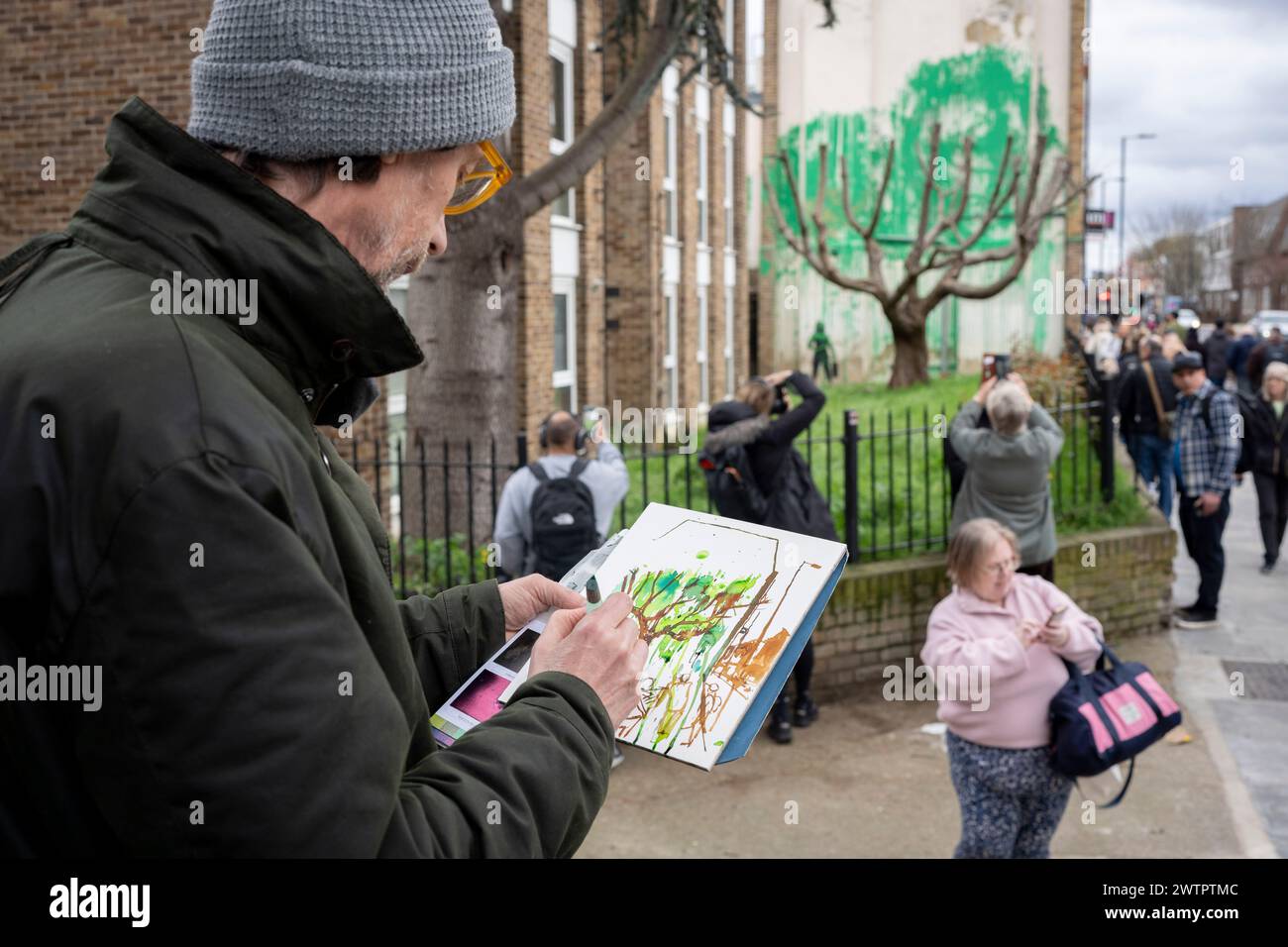 Am 18. März 2024 bewundert die Öffentlichkeit ein neues Kunstwerk des mysteriösen Künstlers Banksy an der Hornsey Road im Norden Londons. Das neue Stück erschien am Wochenende, aber heute beanspruchte der Künstler die Anerkennung für dieses neueste Werk - ein grünes Spray auf einer Wohnwand hinter einem getrimmten Baum, der wie Laub aussieht, mit einer Schablone einer Person, die einen Druckschlauch daneben hält. Stockfoto