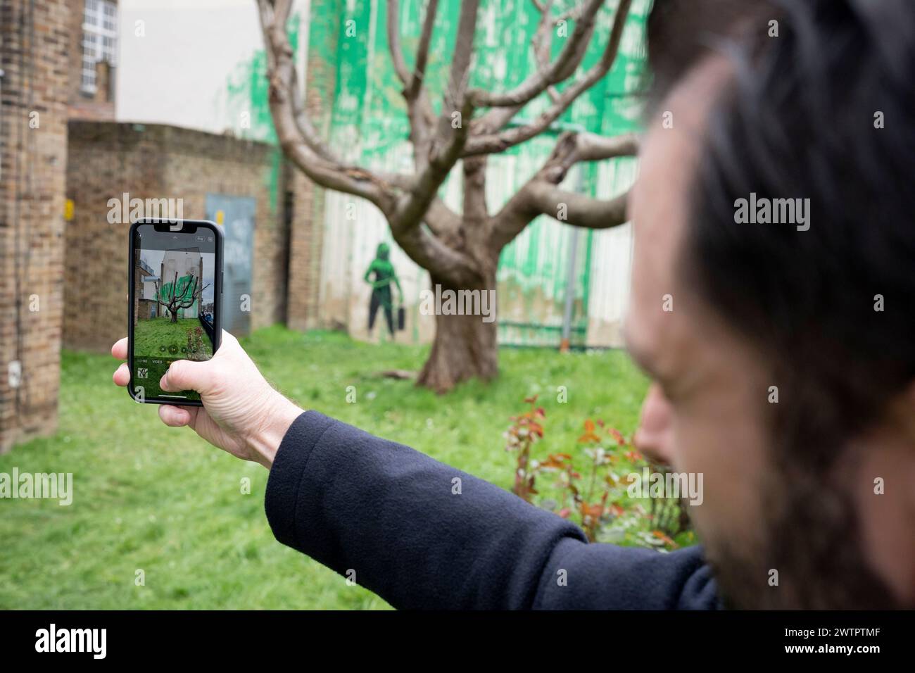 Am 18. März 2024 bewundert die Öffentlichkeit ein neues Kunstwerk des mysteriösen Künstlers Banksy an der Hornsey Road im Norden Londons. Das neue Stück erschien am Wochenende, aber heute beanspruchte der Künstler die Anerkennung für dieses neueste Werk - ein grünes Spray auf einer Wohnwand hinter einem getrimmten Baum, der wie Laub aussieht, mit einer Schablone einer Person, die einen Druckschlauch daneben hält. Stockfoto