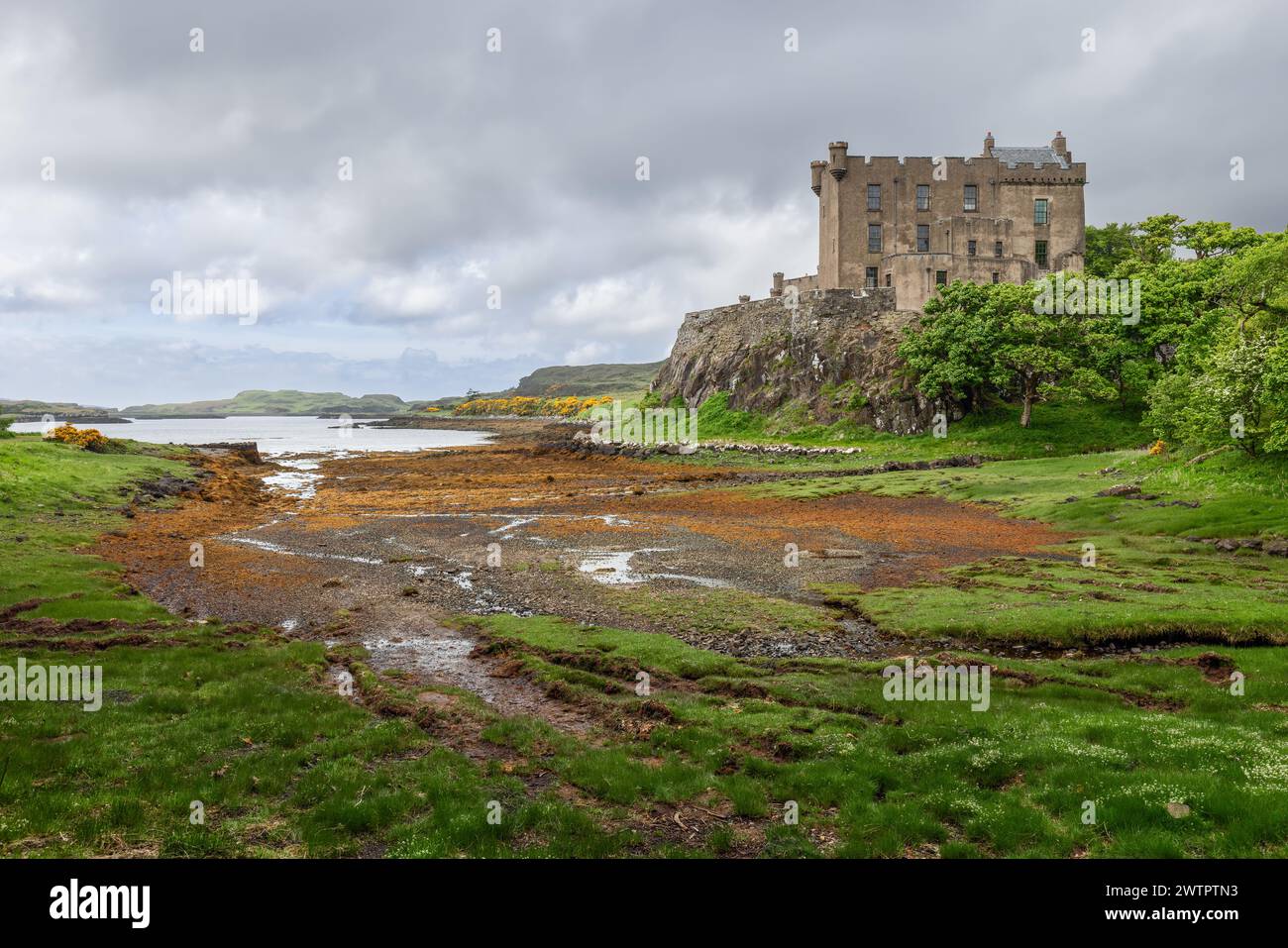 Dunvegan Castle thront auf einer zerklüfteten Klippe und überblickt ein ruhiges Loch mit einer Palette von Grün- und Brandstiften, die die Küste bemalen Stockfoto