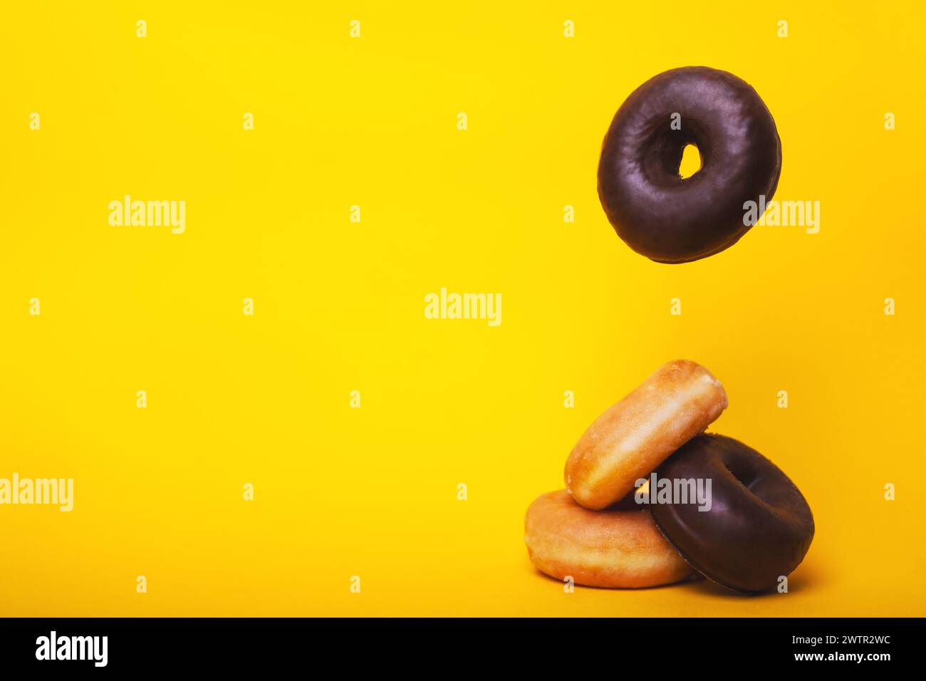 Horizontales Foto von Zucker- und Schokoladenkrapfen, die übereinander fallen, in einem Stapel auf einem leuchtend gelben Hintergrund. Stockfoto