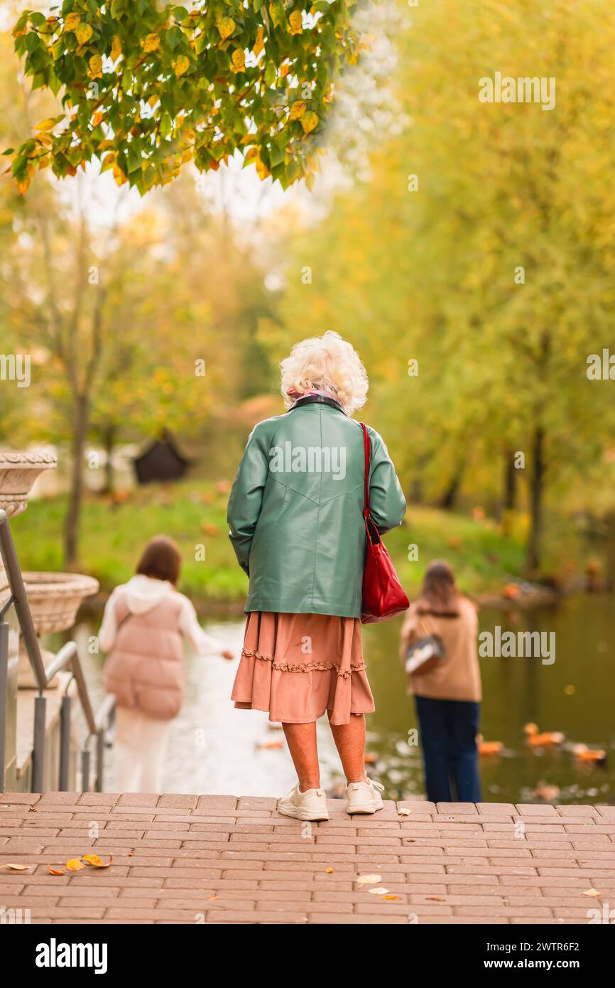 Rückansicht einer älteren Frau mit grauem Haar im Herbstpark. Freizeit, Erholung für ältere Erwachsene Stockfoto