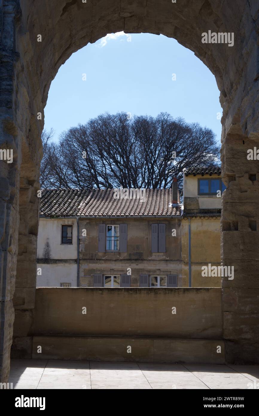Gebäude und Baum durch einen Bogen des Arles Amphitheaters - Arènes d'Arles - ein römisches Amphitheater in Arles Frankreich Stockfoto