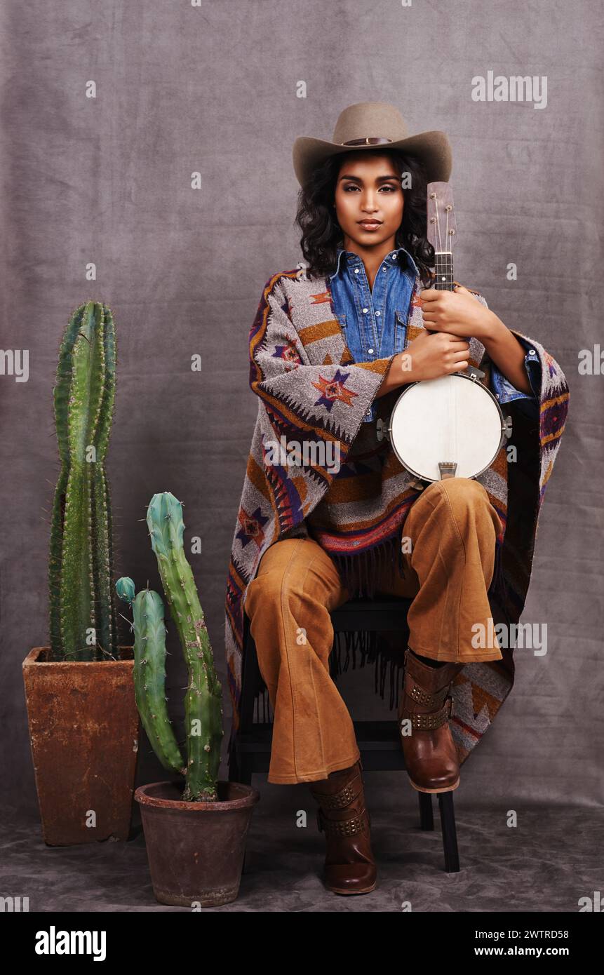 Porträt, Cowgirl oder Frau mit Instrument für Musik im Studio und coole Mode oder Kleidung auf grauem Hintergrund. Amerikanische Ureinwohner, westliche und Stockfoto