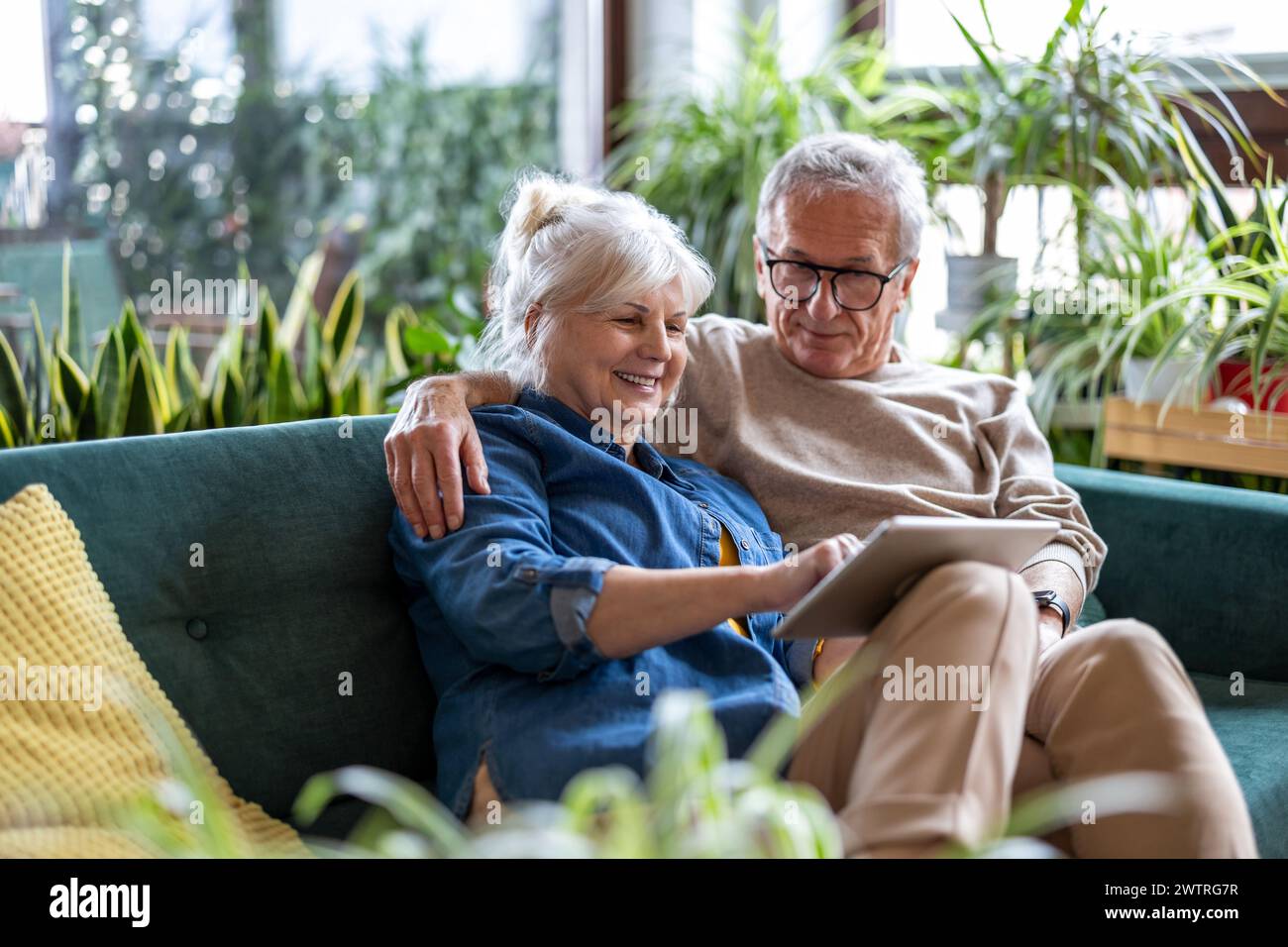 Glückliches Seniorenpaar, das ein digitales Tablet verwendet, während es im Wohnzimmer auf dem Sofa sitzt Stockfoto