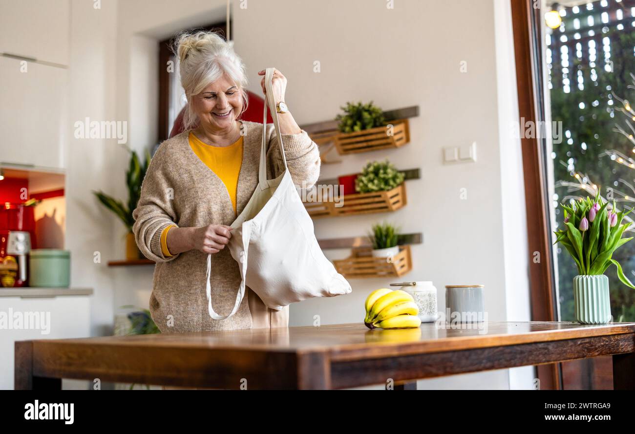 Ältere Frau, die wiederverwendbare Tasche mit Lebensmitteln in der Küche hält Stockfoto