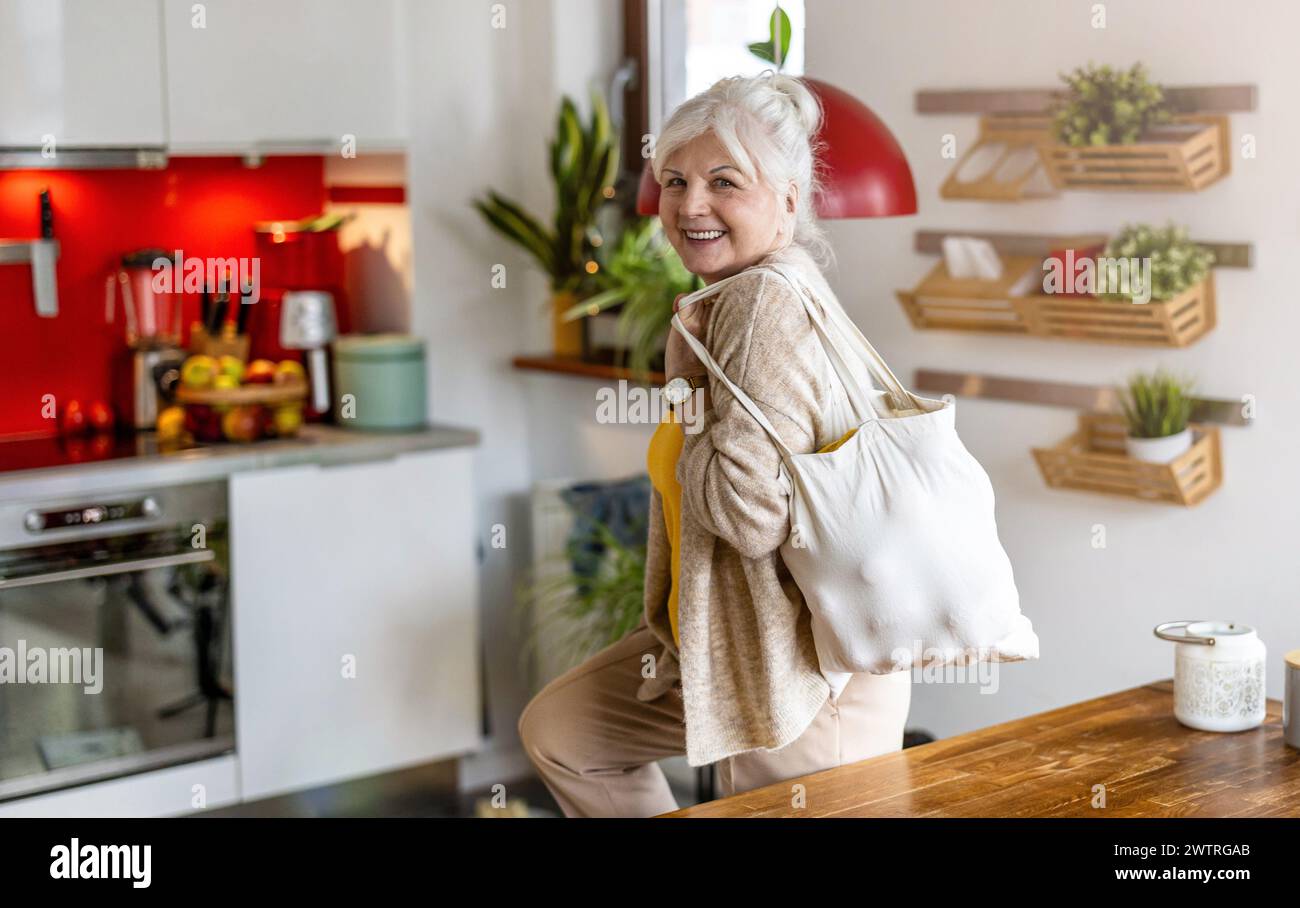 Ältere Frau, die wiederverwendbare Tasche mit Lebensmitteln in der Küche hält Stockfoto