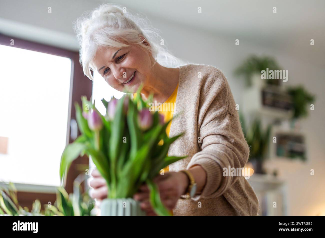 Glückliche Seniorin mit Tulpenstrauß in Vase zu Hause Stockfoto