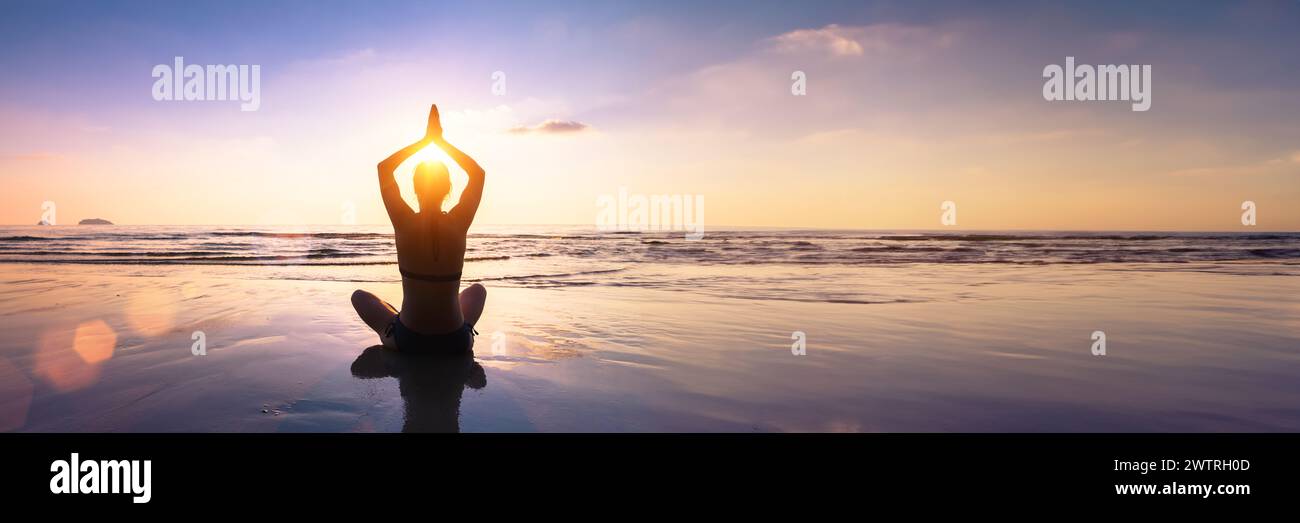 Wohlbefinden und Achtsamkeit durch Yoga-Praxis. Silhouette einer fitten Yogi-Frau in Lotusposition an einem ruhigen Strand bei Sonnenuntergang. Harmonie, Balance, Gelassenheit und Stockfoto