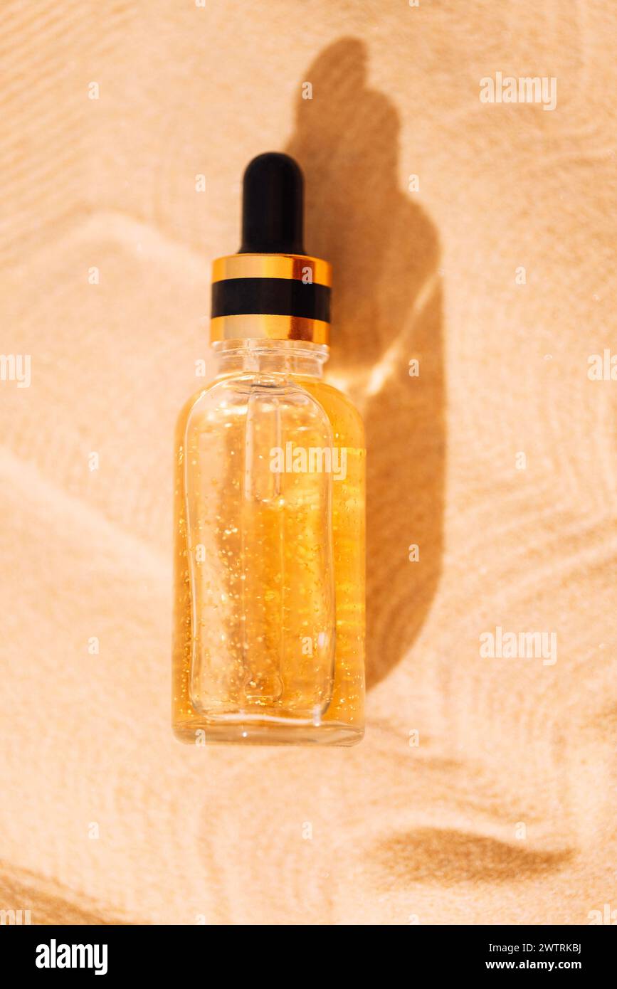 Eine Modell-Glasflasche mit einer Pipette mit einem intensiv feuchtigkeitsspendenden Konzentrat mit Hyaluronsäure und Vitaminen auf einem Hintergrund aus Sand. Goldener Glitt Stockfoto