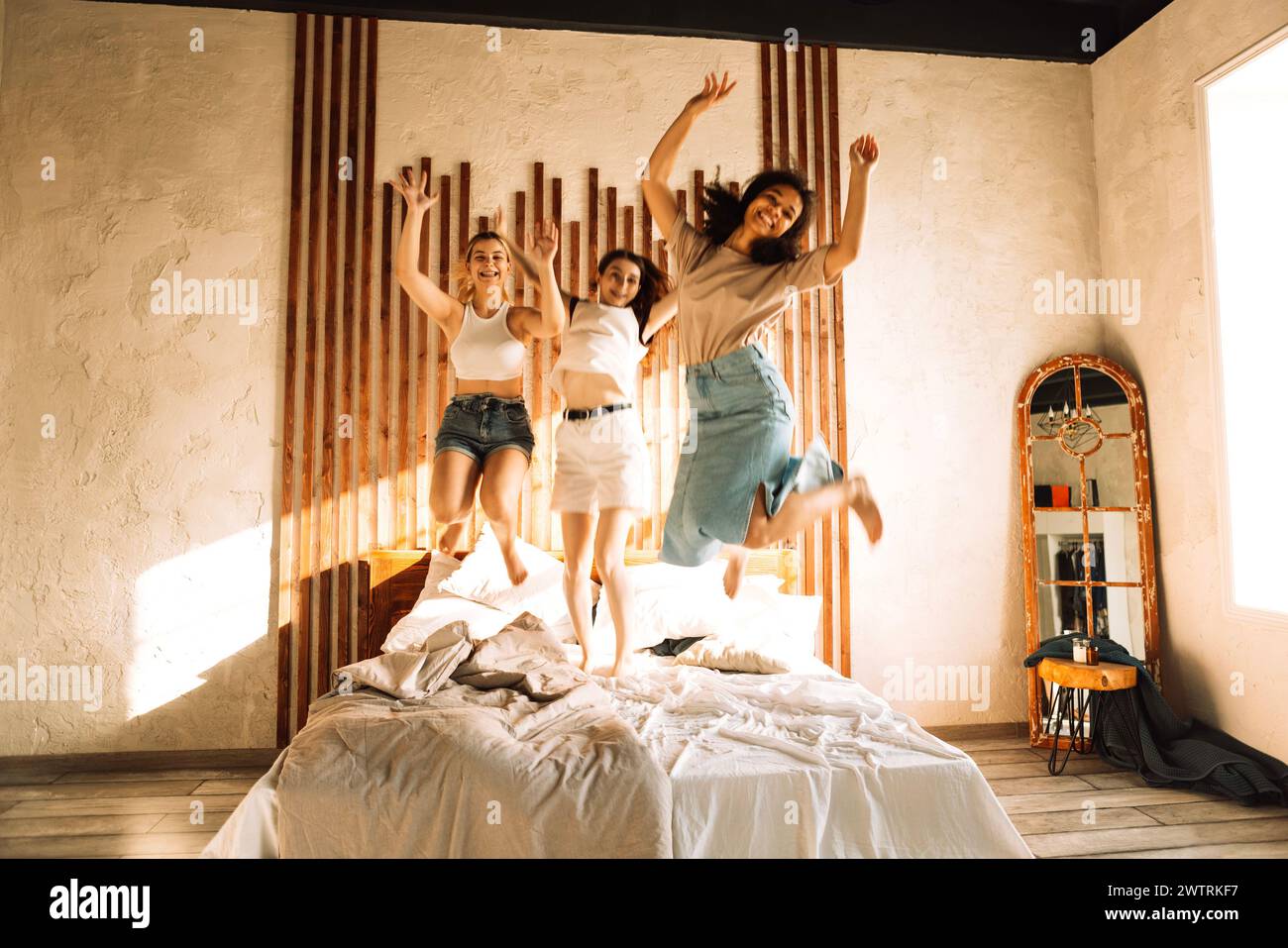 Drei niedliche Teenager-Mädchen verschiedener Rassen springen auf das Bett. Attraktive multiethnische Freundinnen feiern gemeinsam eine Party. Niedliche Schüler Stockfoto