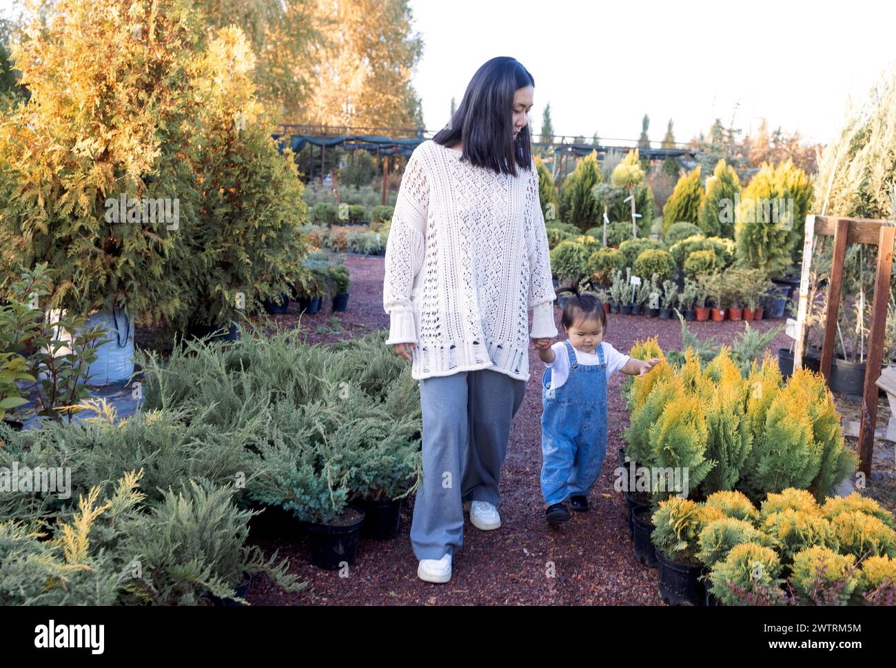 Eine junge Koreanerin und ihre süße Tochter laufen im Garten. Eine asiatische Mutter mit ihrem kleinen Baby sucht sich Setzlinge für ein Zuhause in einer Pflanzenzüchterei aus. Stockfoto