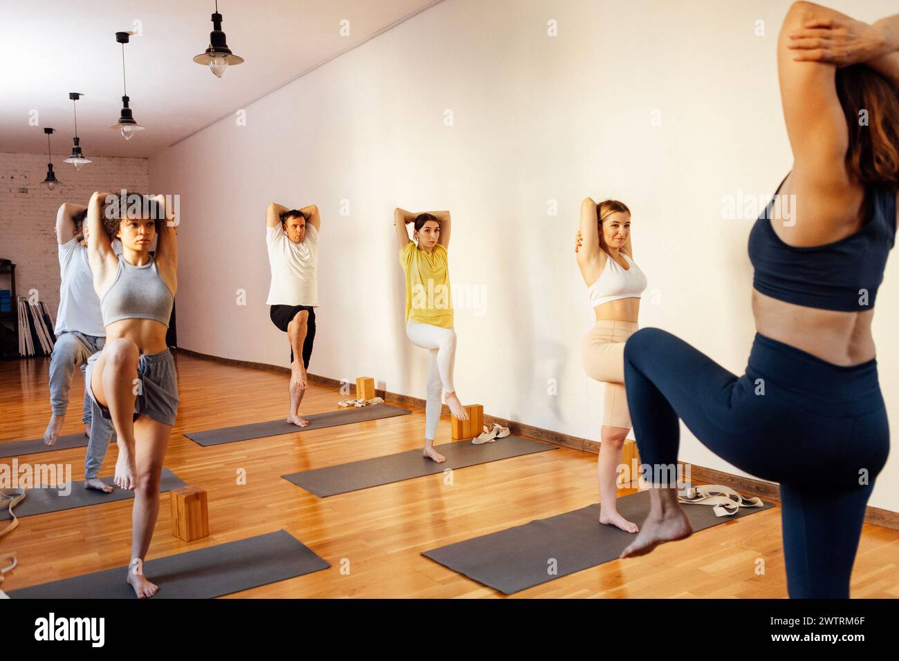 Sportliche Menschen unterschiedlichen Alters und Rassen üben Yoga Asanas mit Trainer im Fitnessclub. Junge multiethnische Frauen und Männer stehen auf Matten und Streten Stockfoto
