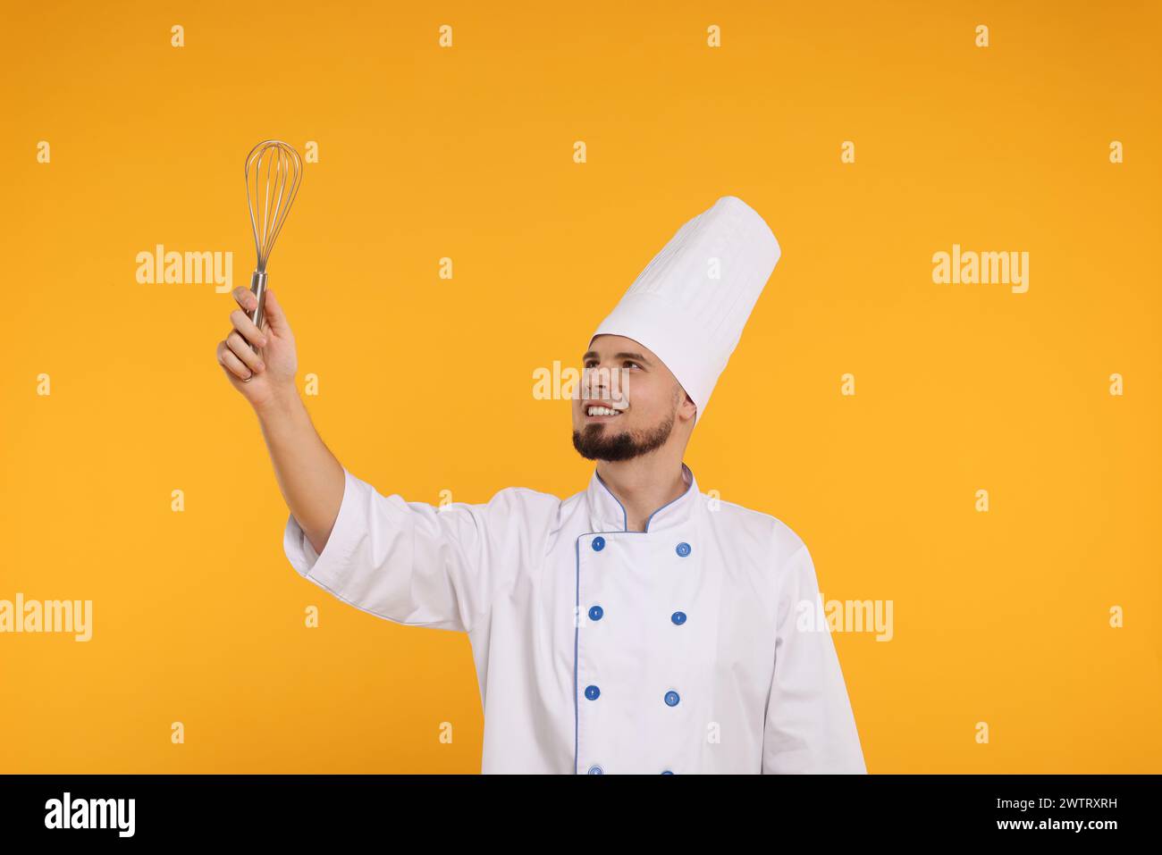 Glücklicher professioneller Konditor in Uniform mit Schneebesen auf gelbem Hintergrund Stockfoto