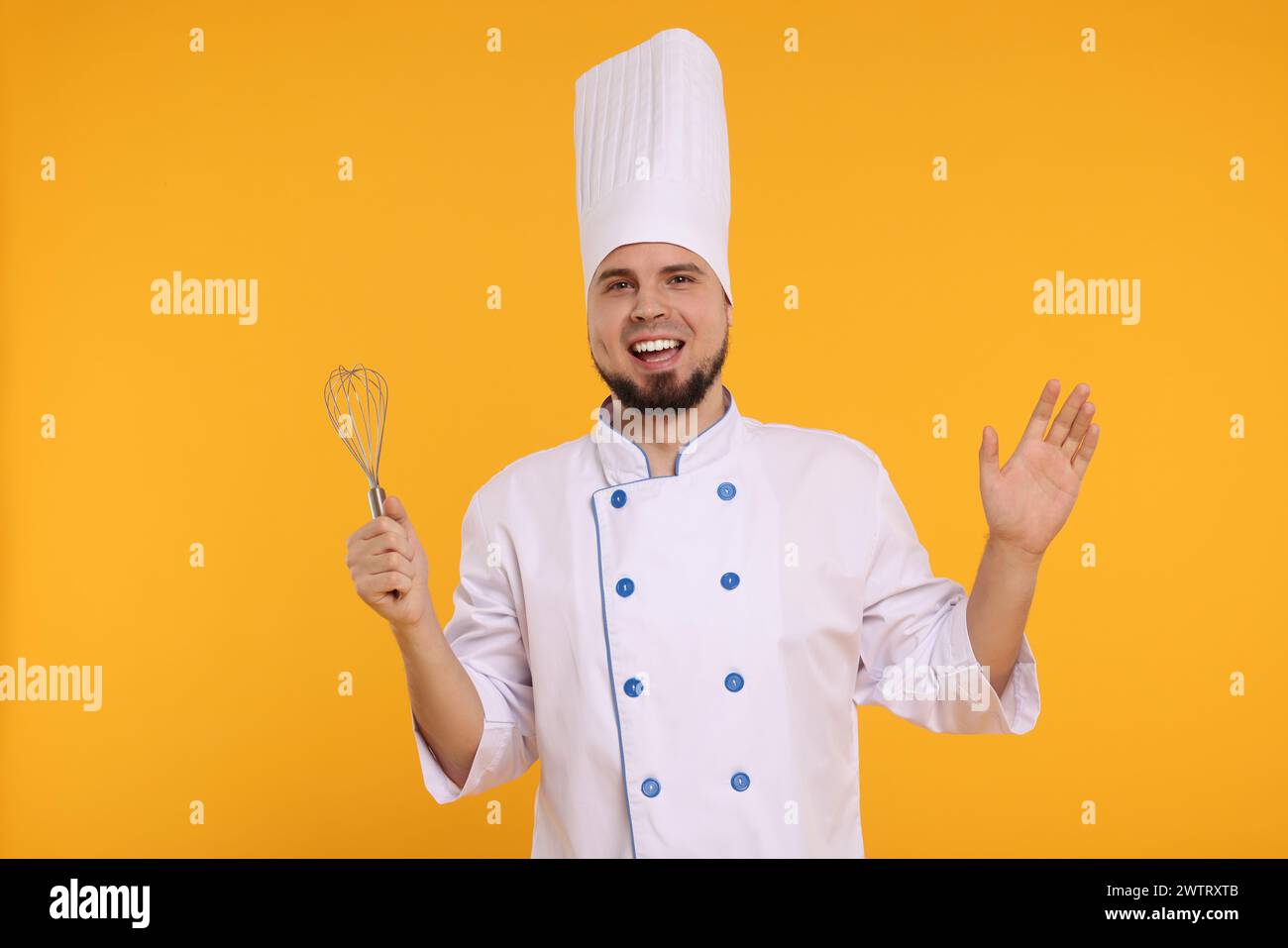 Glücklicher professioneller Konditor in Uniform mit Schneebesen auf gelbem Hintergrund Stockfoto