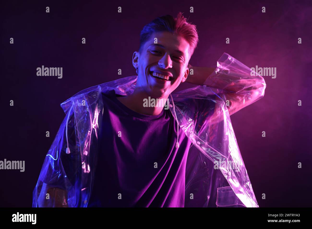 Junger Mann mit klarem Mantel in Neonlichtern mit Raucheffekt Stockfoto