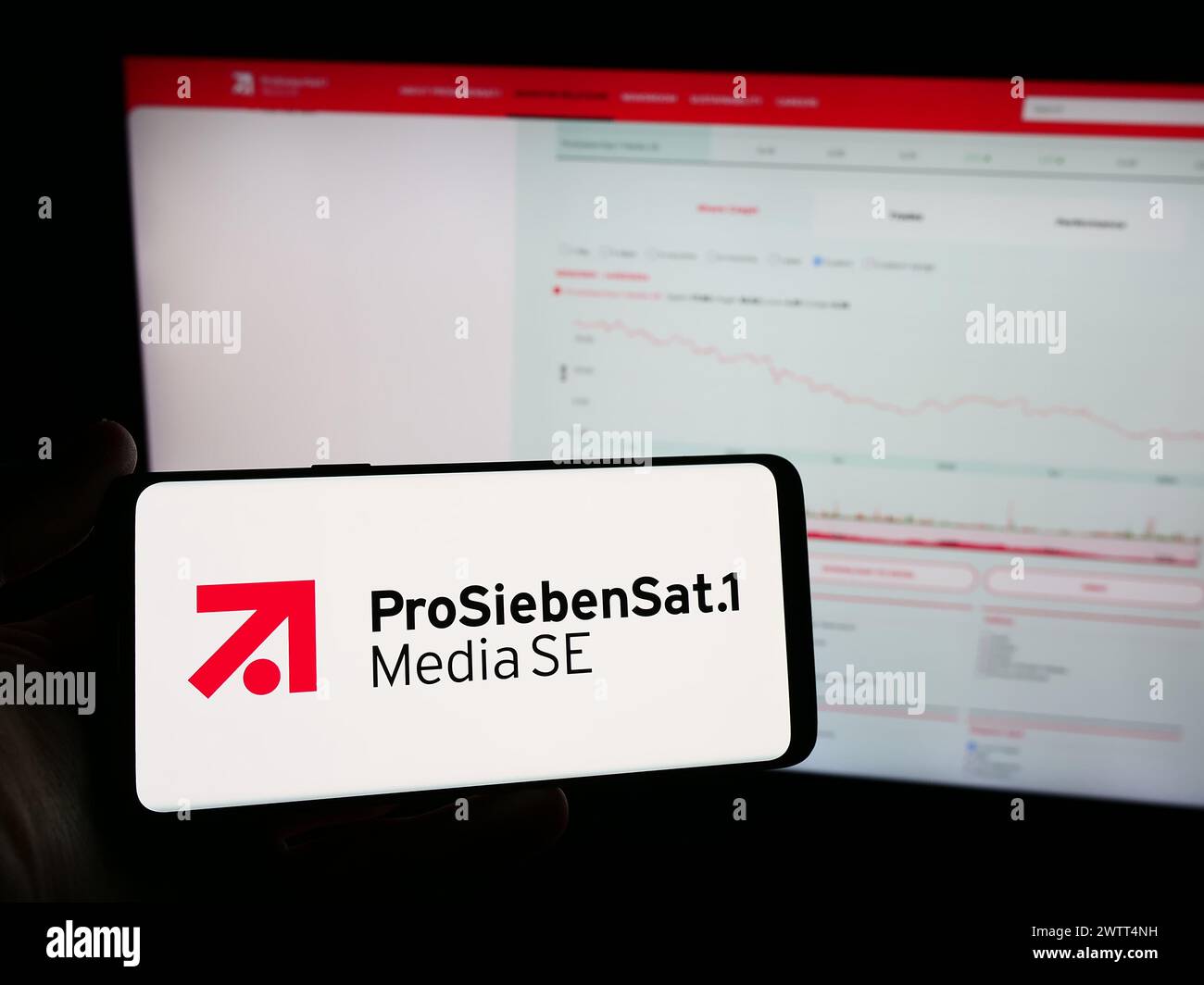 Person mit Mobiltelefon mit Logo der deutschen Fernsehgesellschaft ProSiebenSat.1 Media SE vor der Business-Webseite. Schwerpunkt auf dem Display des Telefons. Stockfoto