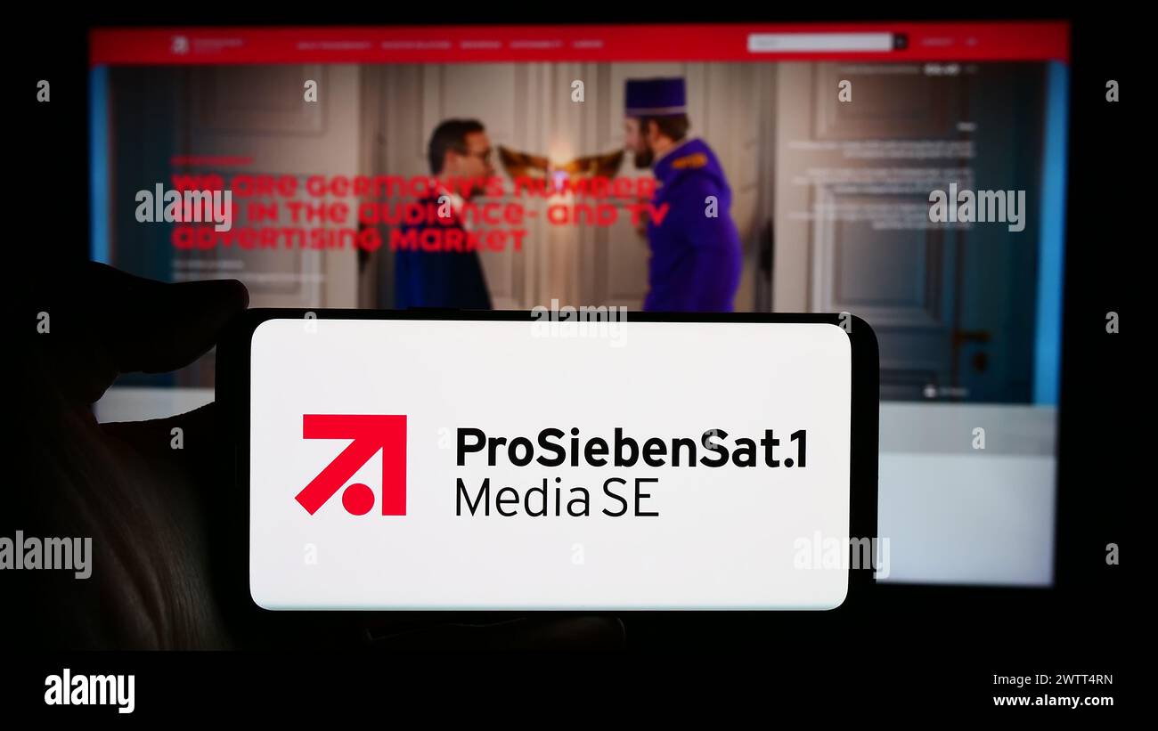 Person mit Mobiltelefon mit Logo der deutschen Fernsehgesellschaft ProSiebenSat.1 Media SE vor der Business-Website. Schwerpunkt auf dem Display des Telefons. Stockfoto