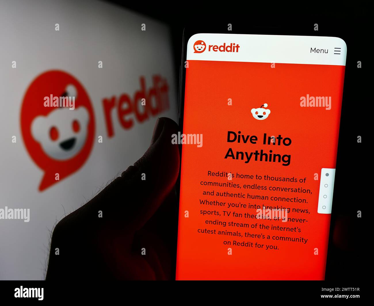Person, die ein Mobiltelefon hält, mit der Webseite des US-amerikanischen Social-Media-Unternehmens Reddit Inc. Vor dem Firmenlogo. Konzentrieren Sie sich auf die Mitte des Telefondisplays. Stockfoto