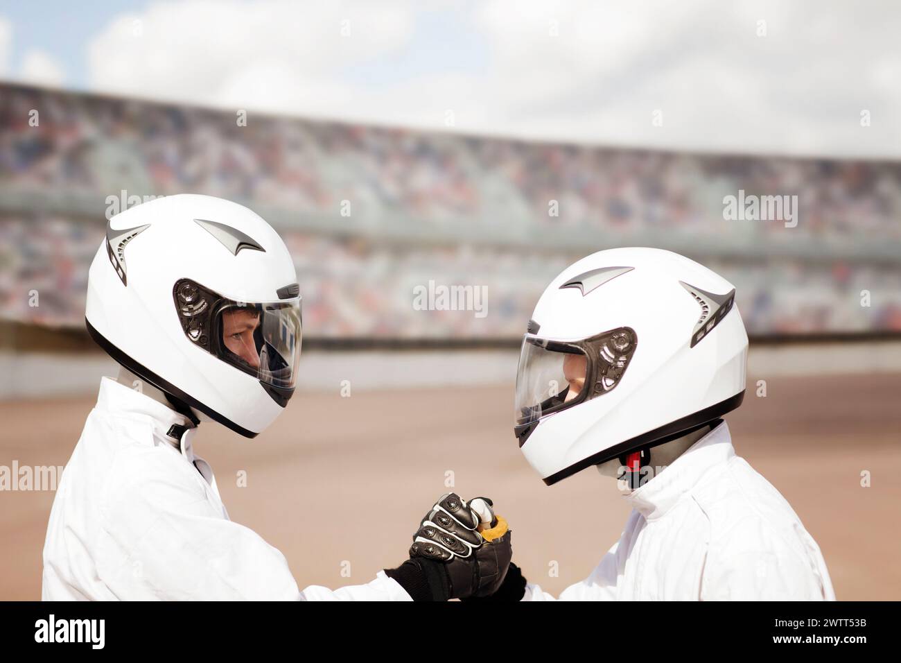 Zwei Motorradfahrer in weißen Anzügen und Helmen teilen sich vor dem Rennen eine Faustwelle. Stockfoto