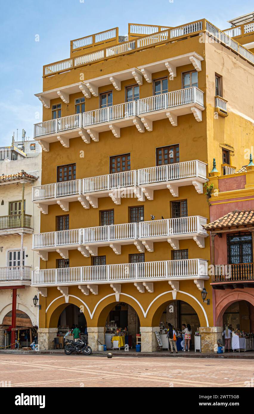 Cartagena, Kolumbien - 25. Juli 2023: 7-stöckiges Gebäude mit gelber Fassade an der Plaza de los Coches ist ein Einkaufszentrum und Apartments. Fußgänger präsentieren sich in Sch Stockfoto