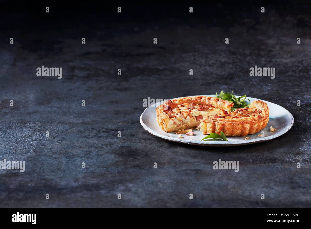 Herzhafte Quiche-Scheibe auf einem rustikalen Teller mit frischen Kräutern Stockfoto