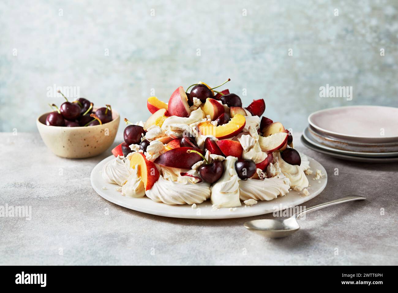 Ein herrlicher pavlova mit saftigen Kirschen und Pfirsichen vor einer ruhigen Kulisse Stockfoto