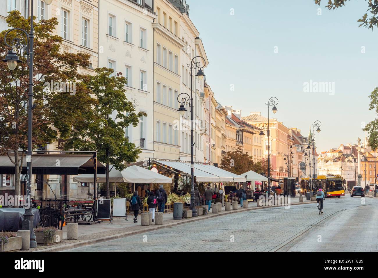 Golden Hour über einer belebten Stadtstraße, gesäumt von Cafés und historischer Architektur. Stockfoto