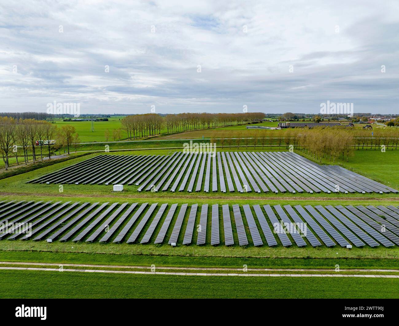 Weitläufiger Solarpark, der sich über eine grüne Landschaft unter bewölktem Himmel erstreckt. Stockfoto