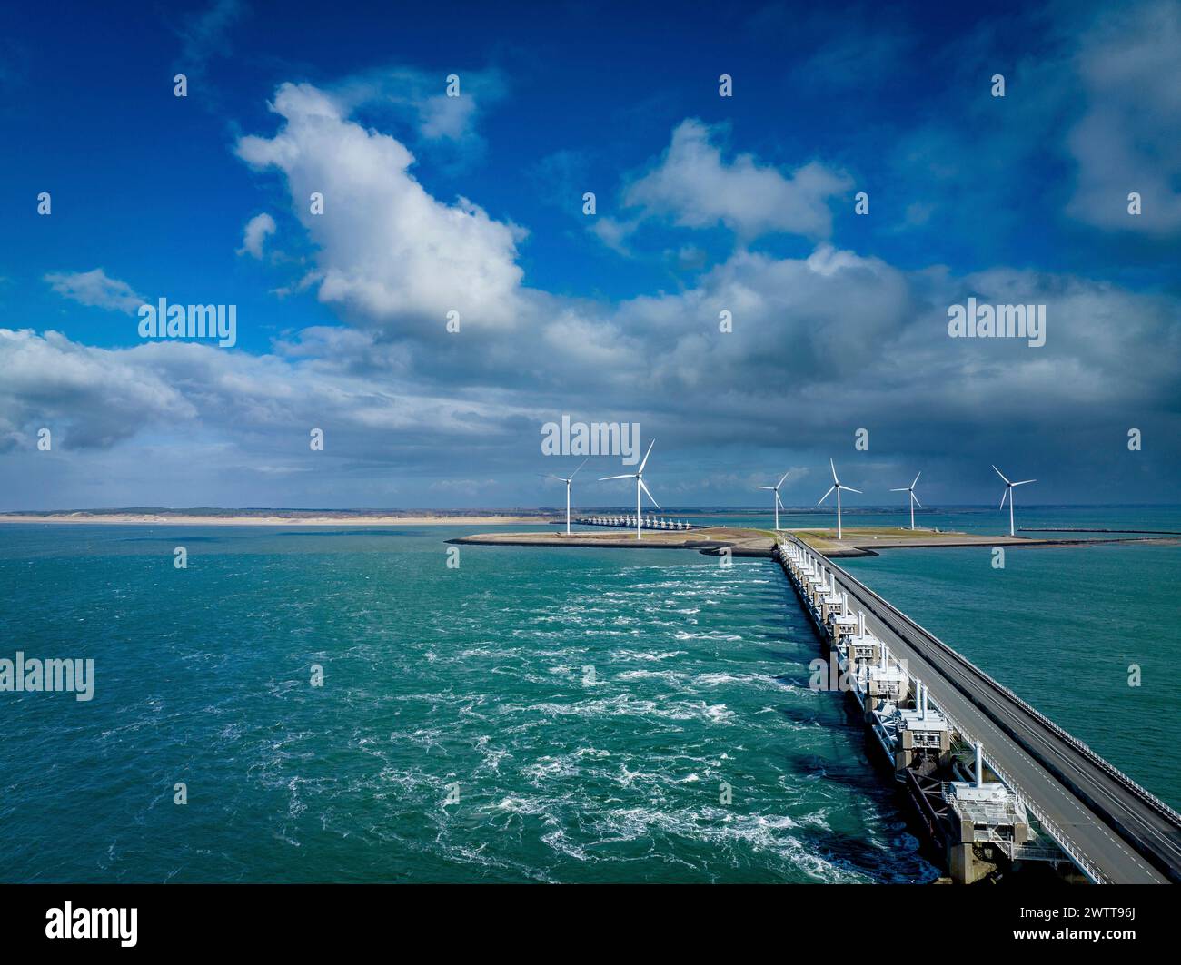 Ein malerischer Blick auf einen Pier, der zu einem Windpark an der Küste unter einem hellblauen Himmel führt. Stockfoto