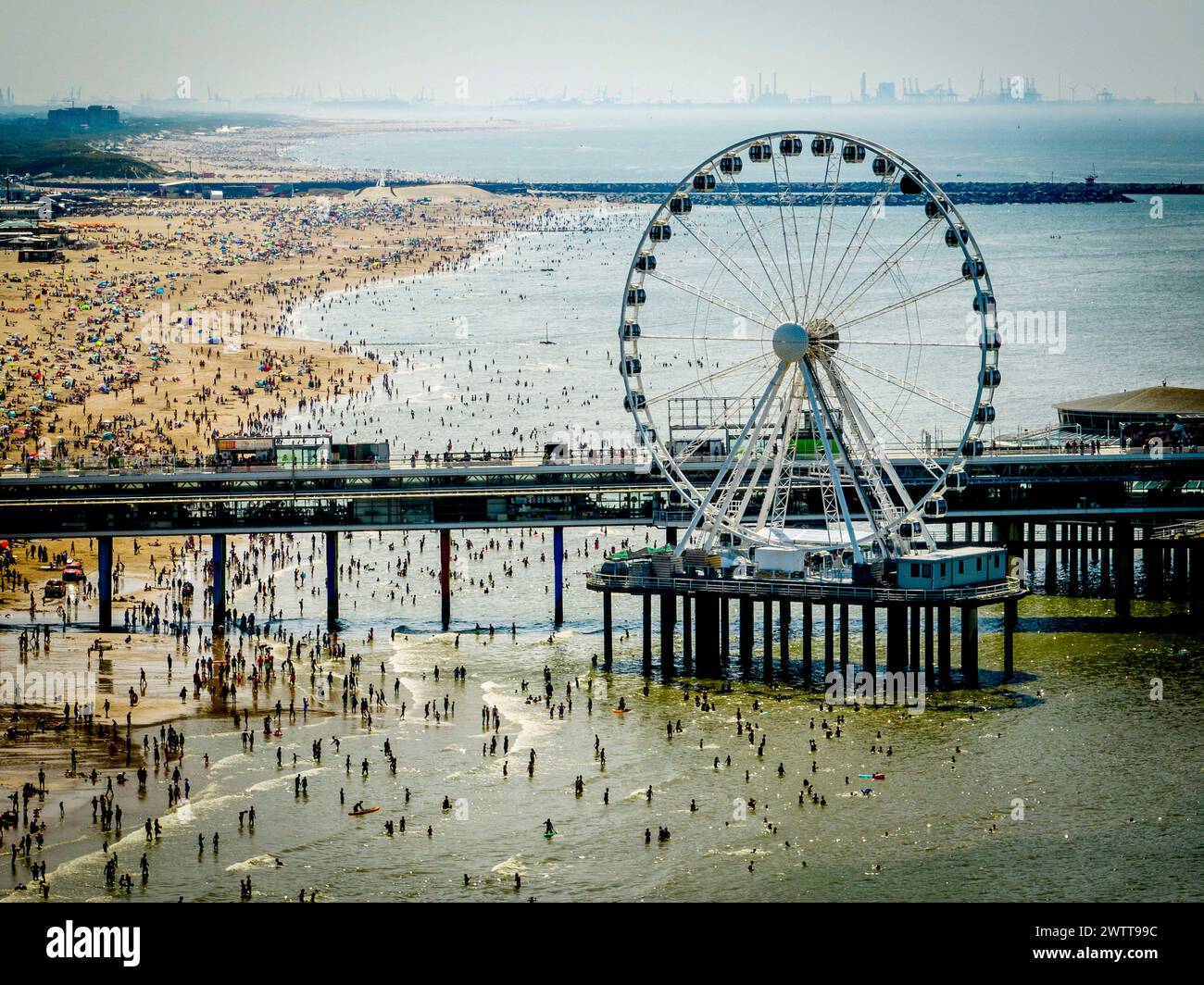 Belebter Strandtag mit einem Riesenrad hoch über dem Pier Stockfoto