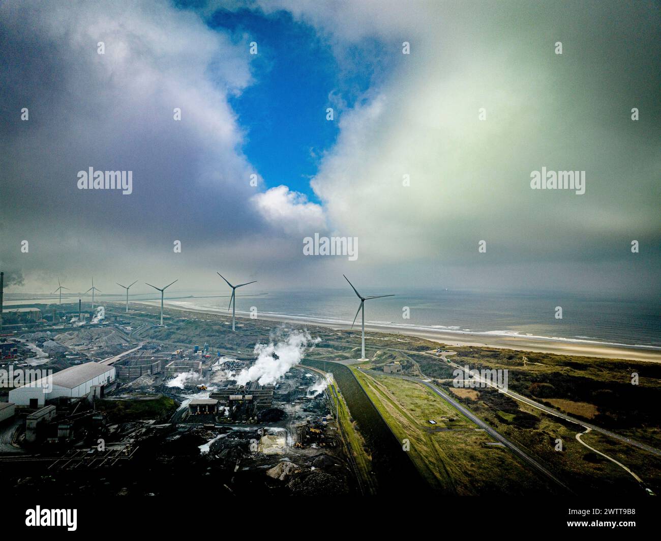 Ein stimmungsvoller Blick aus der Luft auf ein Industriegebiet an der Küste mit Windturbinen und dramatischen Wolken. Stockfoto