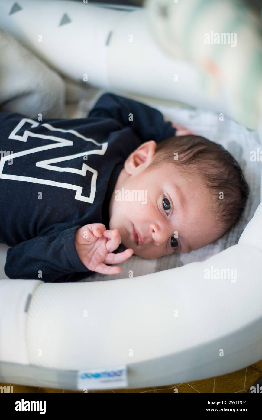 Ein neugeborenes Baby blickt neugierig, während es in einer gemütlichen Wanne ruht. Stockfoto