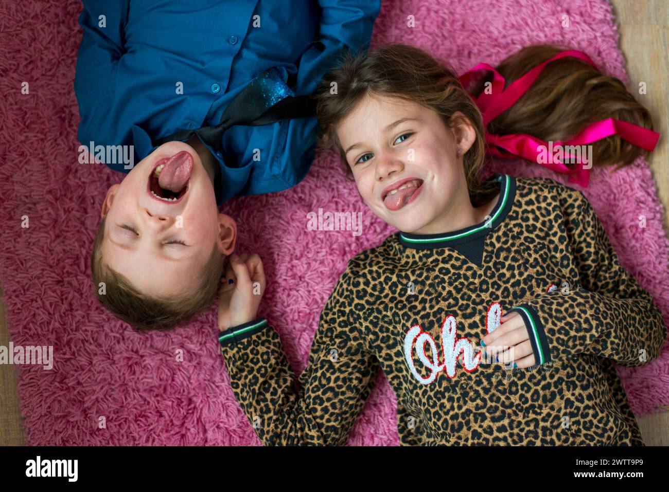 Zwei Kinder teilen sich einen fröhlichen Moment auf einem gemütlichen rosafarbenen Teppich. Stockfoto
