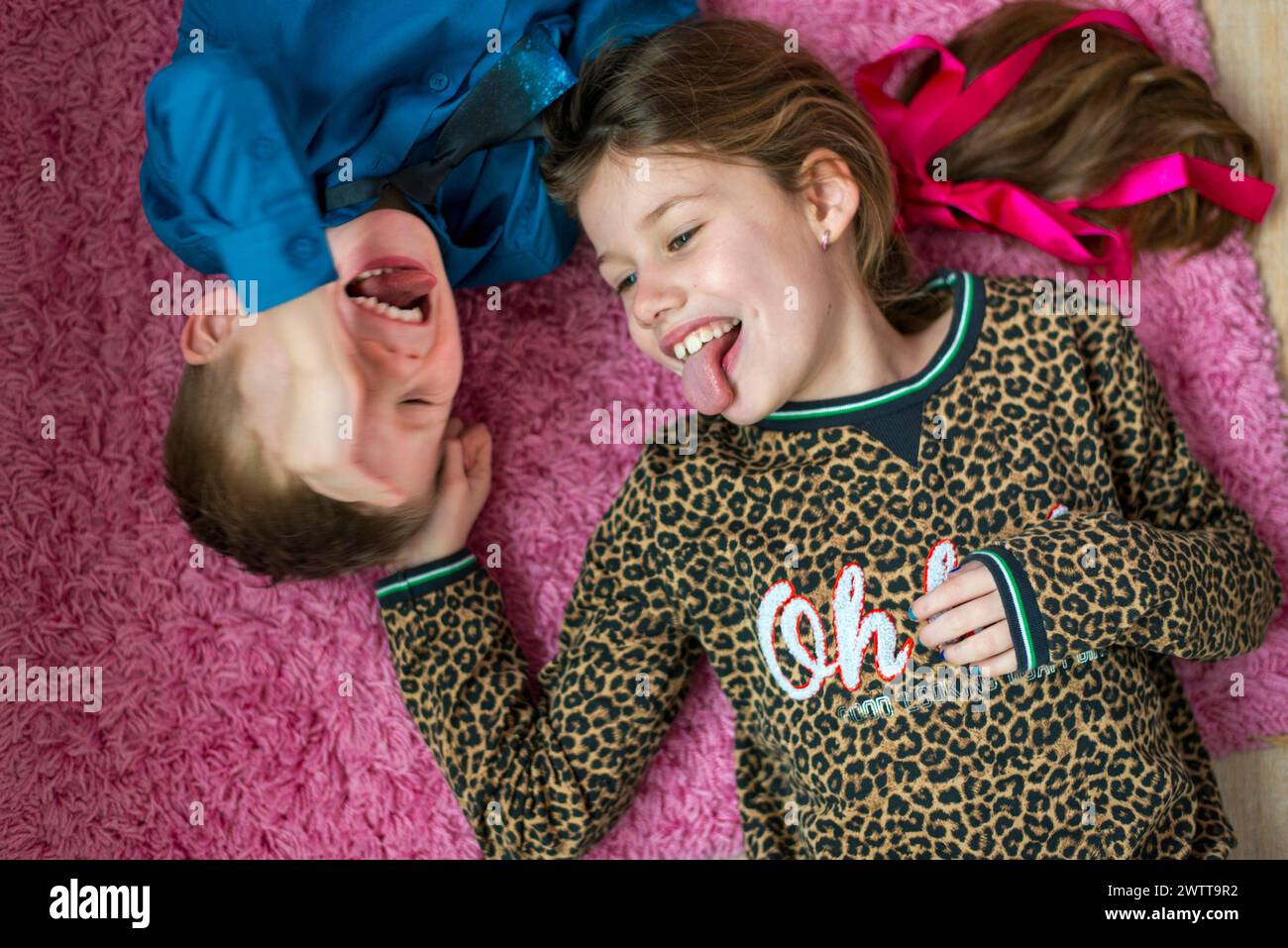 Zwei Kinder machen lustige Gesichter, während sie auf einem rosa Teppich liegen. Stockfoto