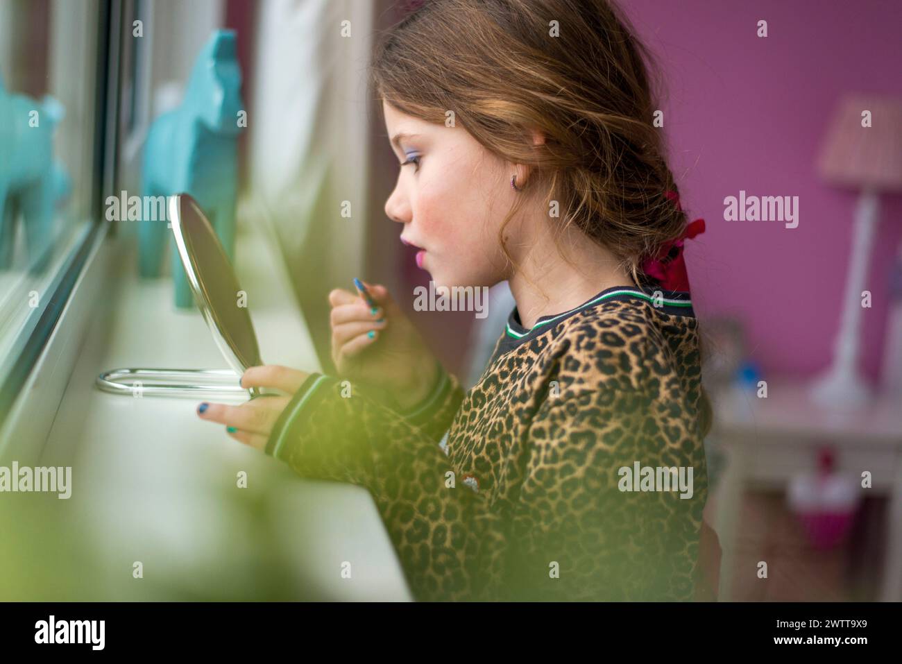 Ein junges Mädchen hat sich darauf konzentriert, Make-up am Fenster aufzutragen Stockfoto