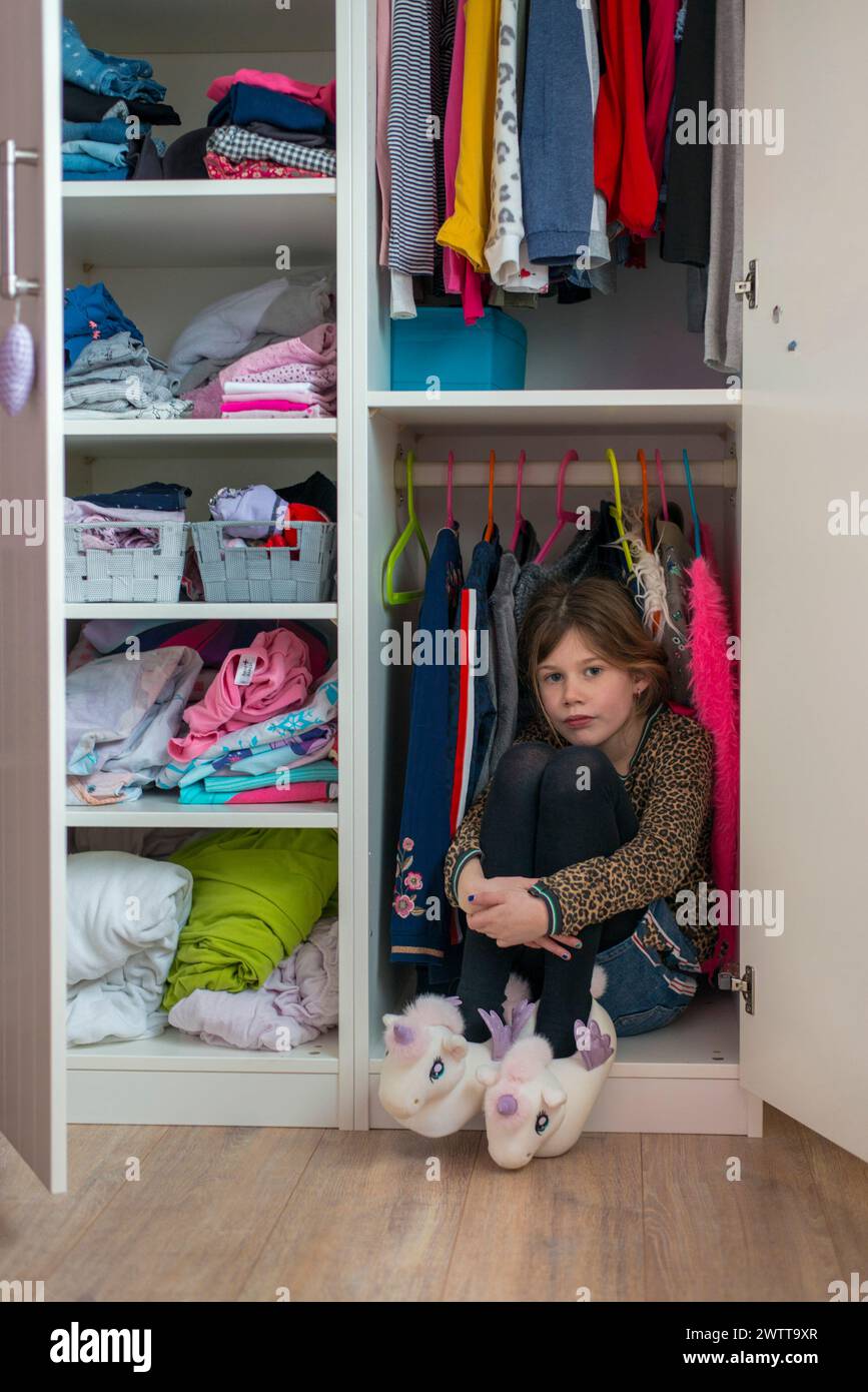 Kleines Mädchen, das sich in einem bunten Kleiderschrank versteckt Stockfoto