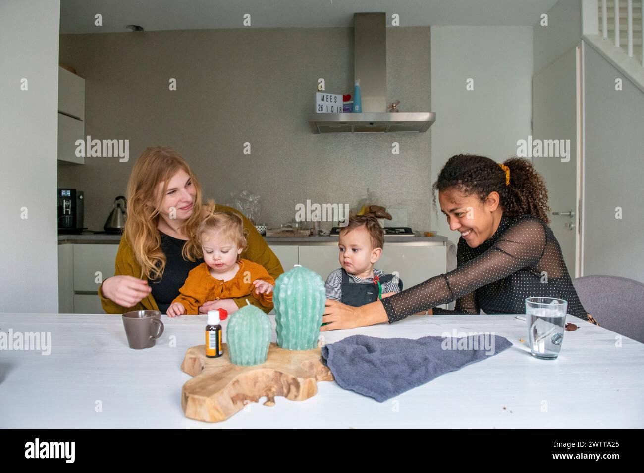 Familienspaß, während zwei Erwachsene mit Kleinkindern an einem gemütlichen Küchentisch spielen. Stockfoto