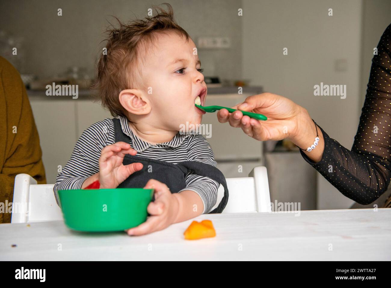 Ein Kleinkind genießt die Mahlzeiten, die von einem Erwachsenen gefüttert werden Stockfoto