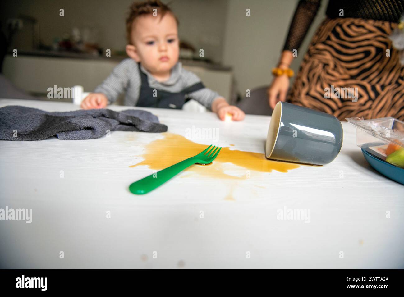 Ein neugieriges Kleinkind schaut auf ein verschüttetes Getränk auf einem Tisch. Stockfoto