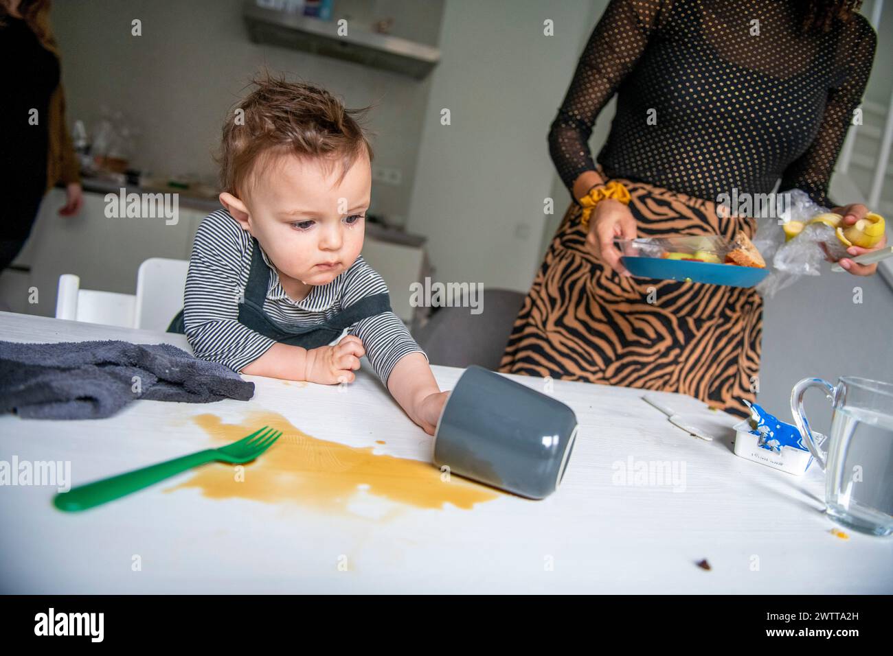 Ein neugieriges Kleinkind erkundet die Nachwirkungen eines verschütteten Getränks zu Hause. Stockfoto