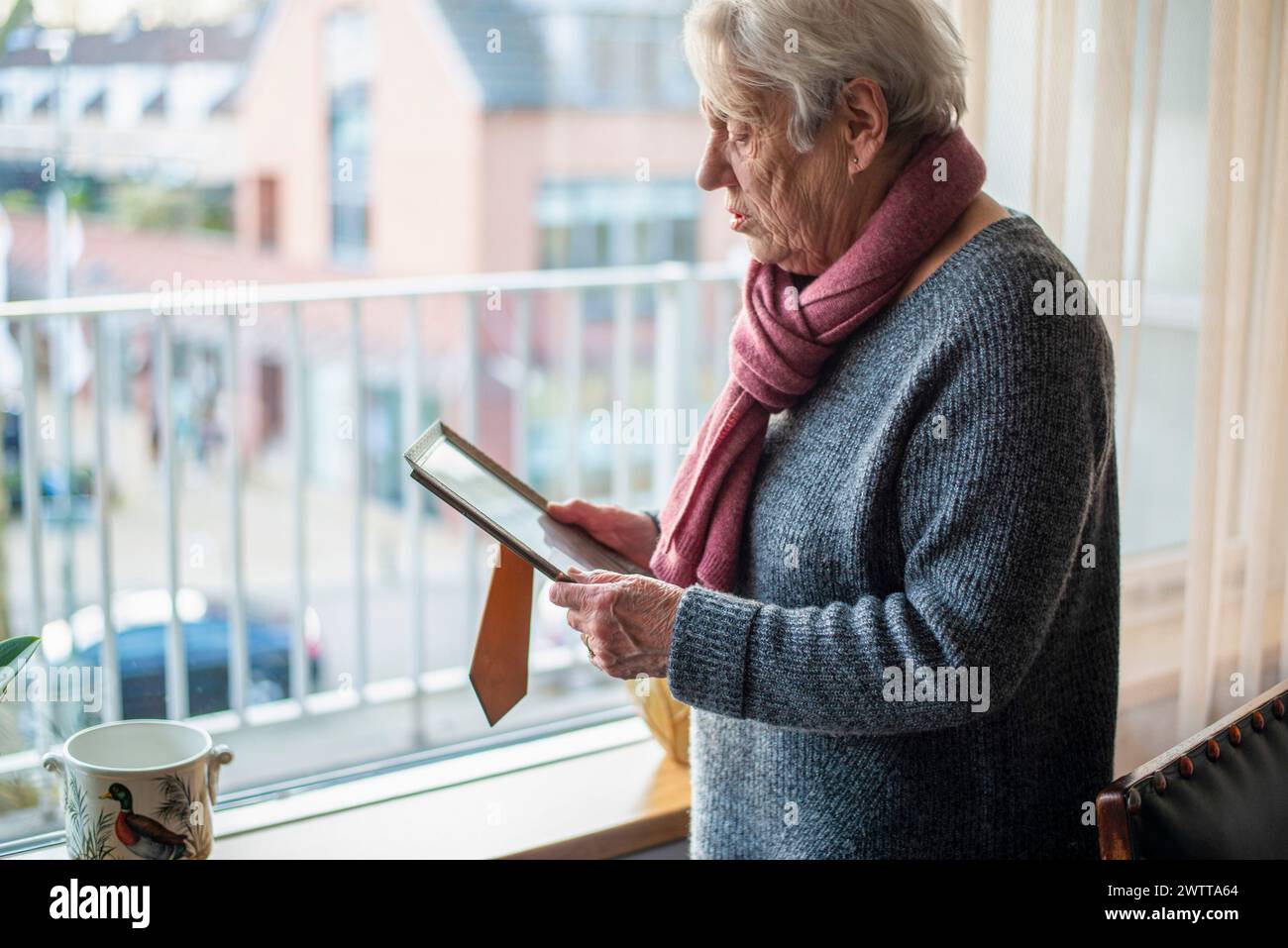 Älterer Mensch, der mit kontemplativem Blick am Fenster liest Stockfoto