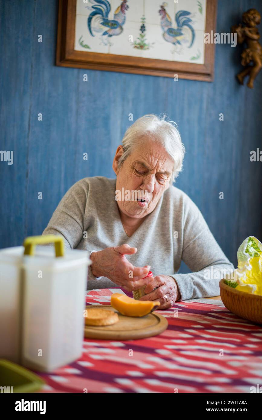 Ältere Person schält eine Orange am Küchentisch. Stockfoto