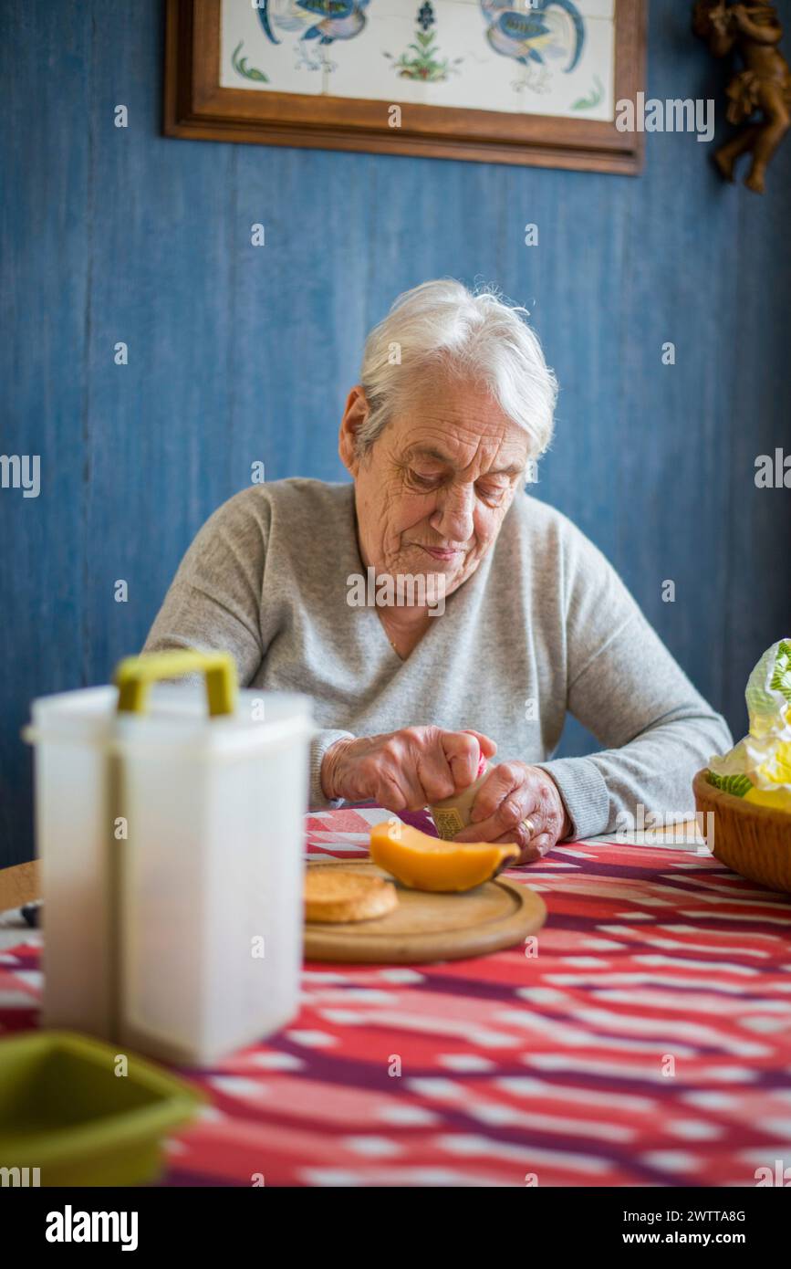 Ältere Person, die eine Orange an einem gemütlichen Küchentisch schneidet. Stockfoto
