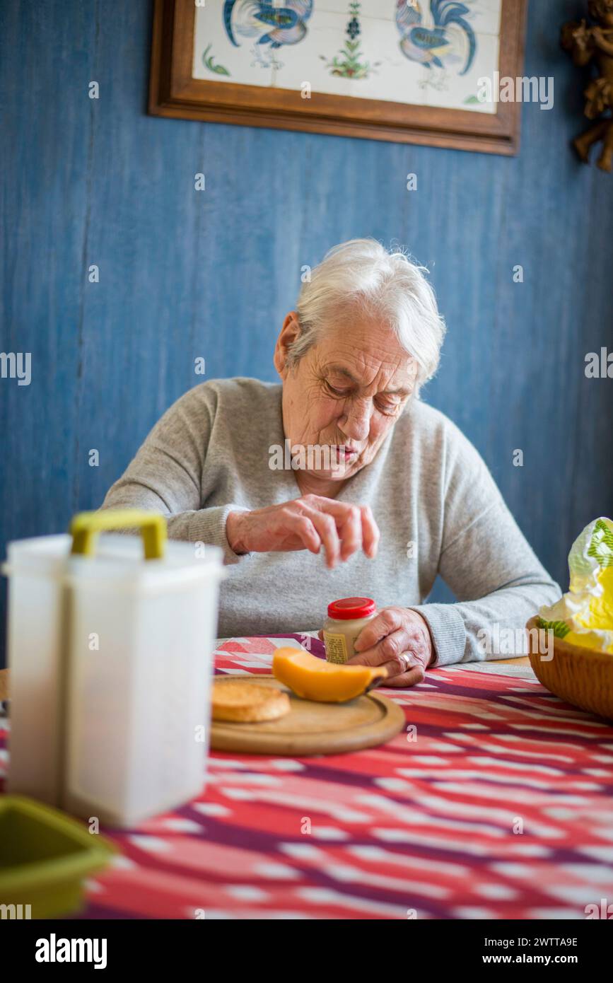 Ein älterer Mensch sitzt an einem Esstisch und konzentriert sich darauf, ein Glas zu öffnen. Stockfoto