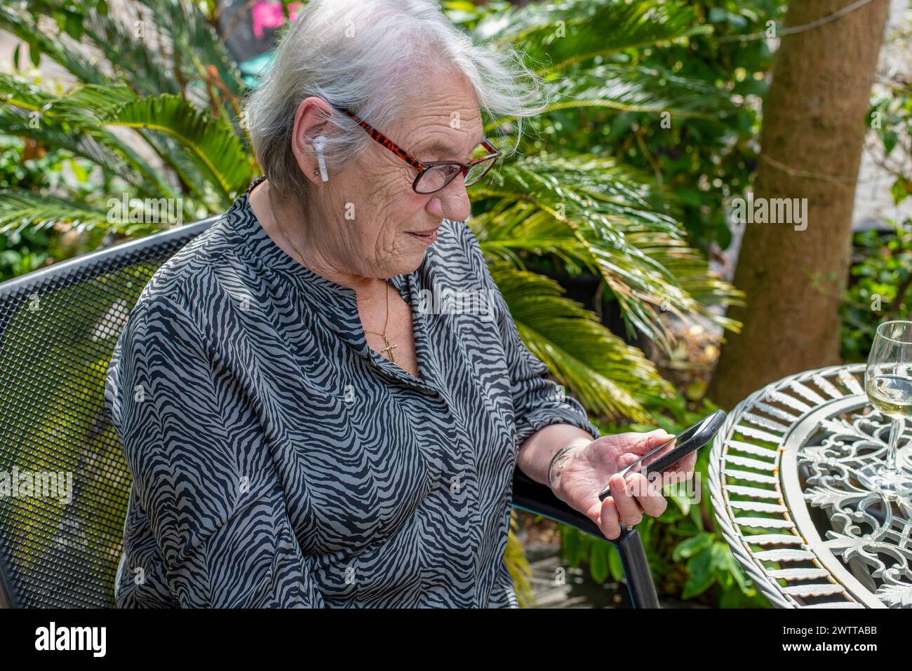 Ältere Dame genießt Technologie in einem Garten Stockfoto