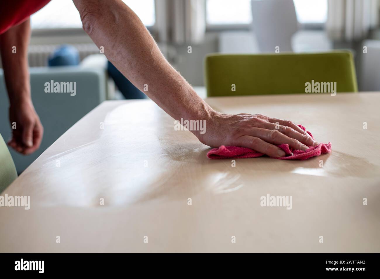 Eine Person, die in einem hellen Raum mit einem rosa Tuch einen Tisch abwischt. Stockfoto