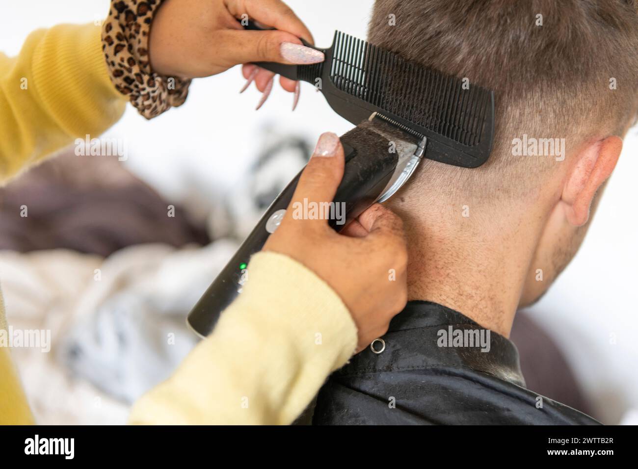 Eine Person erhält einen Haarschnitt von einem Friseur mit einem elektrischen Haarschneider und einem Kamm. Stockfoto