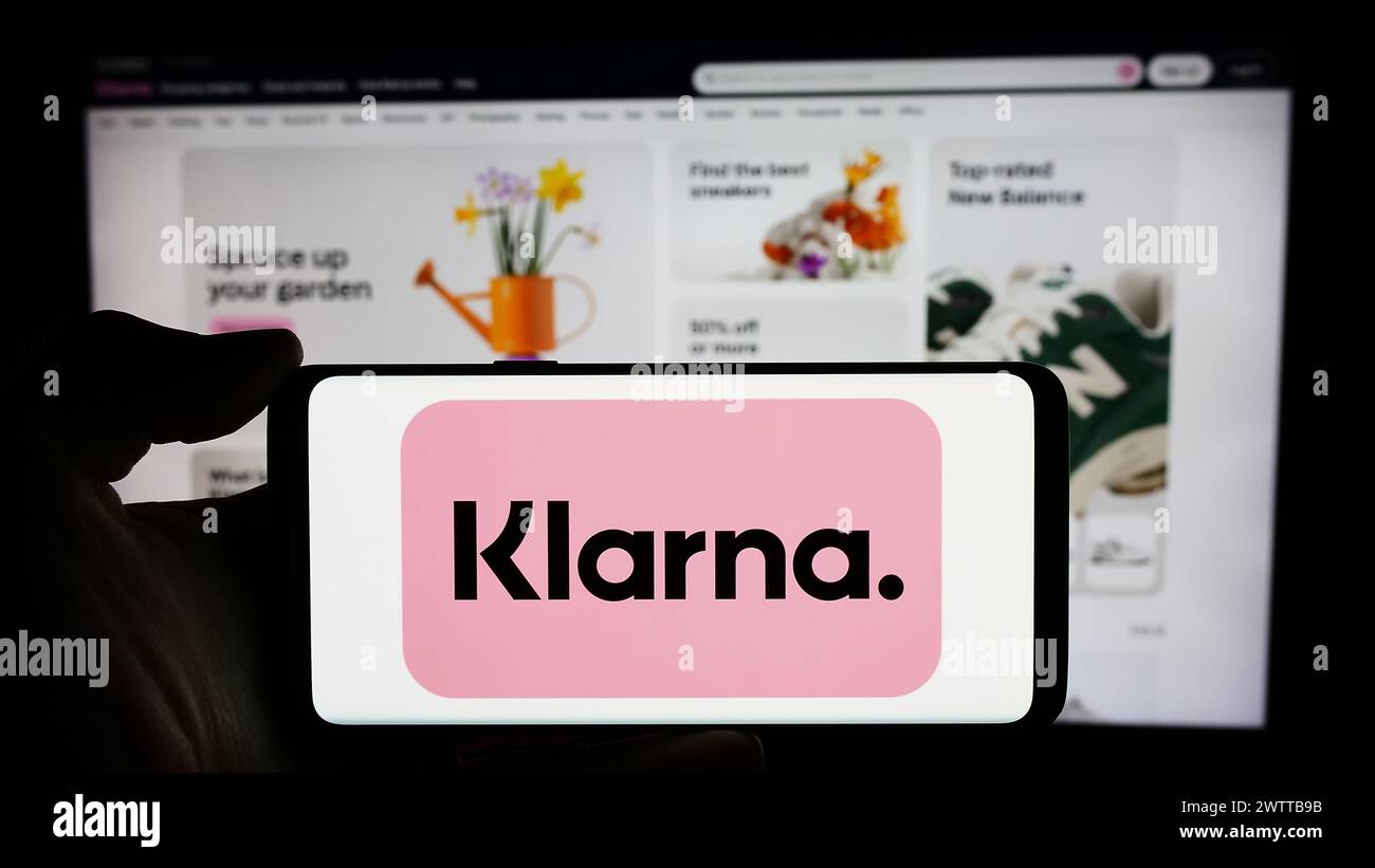 Person, die ein Mobiltelefon mit dem Logo des schwedischen Fintech-Unternehmens Klarna Bank ab vor der Business-Webseite hält. Schwerpunkt auf dem Display des Telefons. Stockfoto