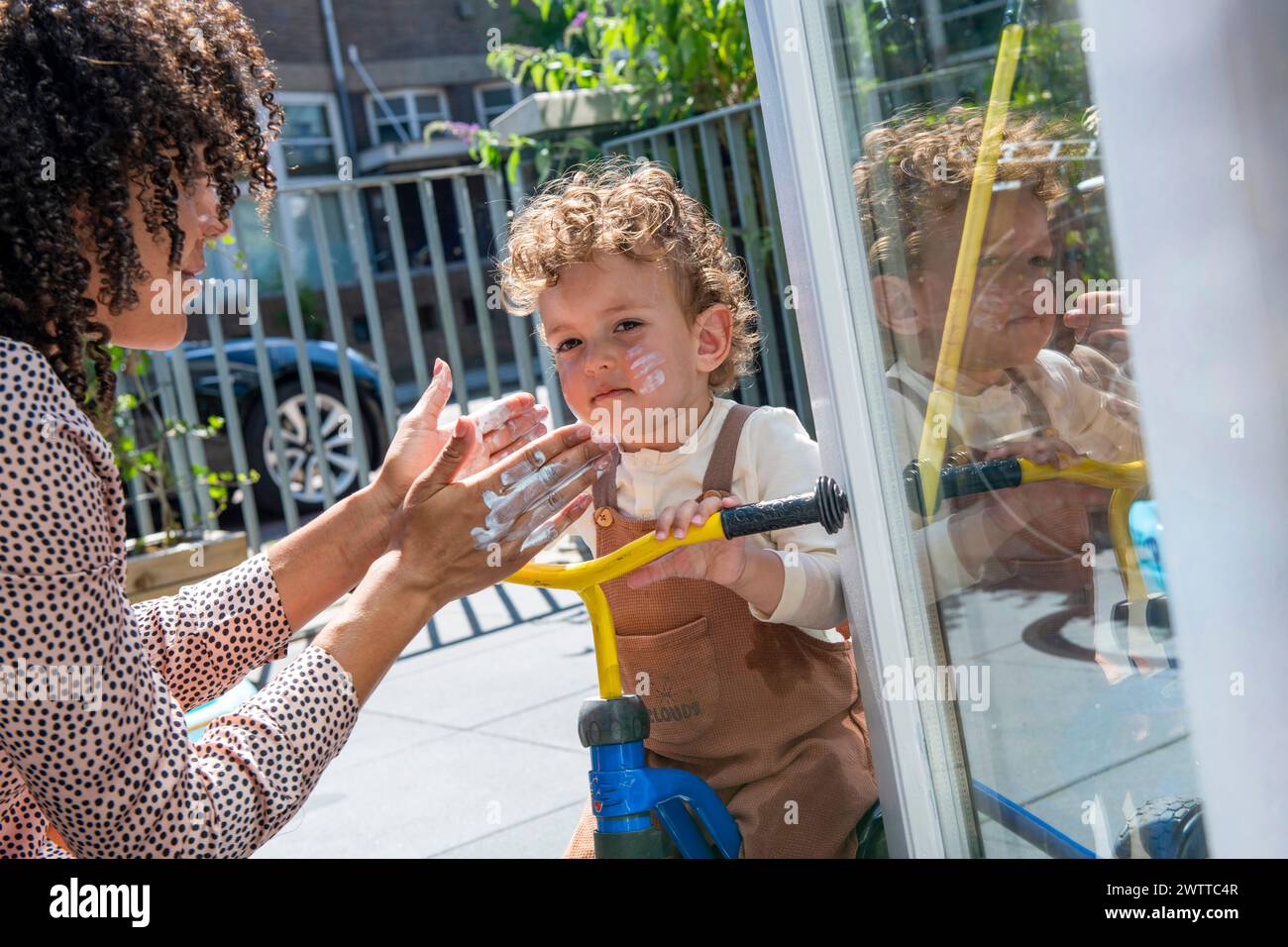 Ein Kind beobachtet aufgeregt durch eine Glastür, während ein Erwachsener an einem sonnigen Tag Gesten macht. Stockfoto